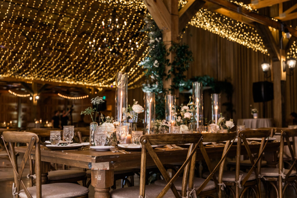 Glamorous fall wedding with timeless floral design and flower colors in white, cream, blush, and black. Bud Vases and candle heavy wedding reception tables create warm ambiance paired with twinkling ceiling lights. Destination wedding in Tennessee countryside. Roses, ranunculus, anemones, and sweet peas. Design by Rosemary & Finch Floral Design in Nashville, TN. 