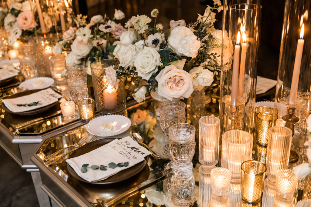 Glamorous fall wedding with timeless floral design and flower colors in white, cream, blush, and black. Lush head table florals and heavy candles create glowing moody environment on these mirror tables for wedding reception. Destination wedding in Tennessee countryside. Roses, ranunculus, anemones, and sweet peas. Design by Rosemary & Finch Floral Design in Nashville, TN. 