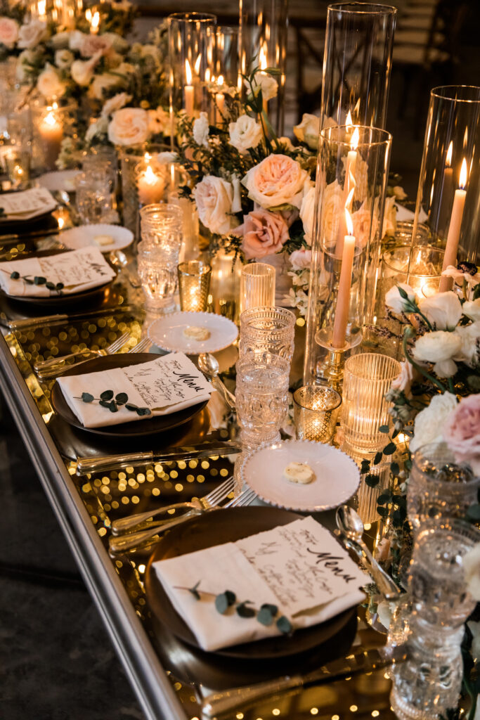 Glamorous fall wedding with timeless floral design and flower colors in white, cream, blush, and black. Lush head table florals and heavy candles create glowing moody environment on these mirror tables for wedding reception. Destination wedding in Tennessee countryside. Roses, ranunculus, anemones, and sweet peas. Design by Rosemary & Finch Floral Design in Nashville, TN. 