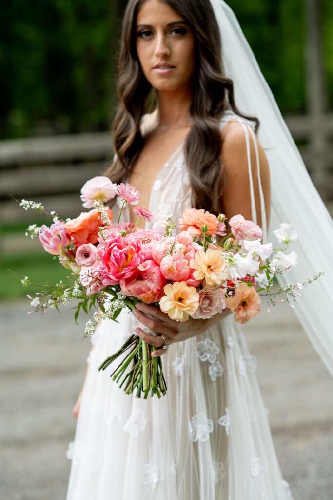 Floral heavy pink bridal bouquet featuring peak spring blooms. Bouquet featuring peonies, tulips, ranunculus, butterfly ranunculus, and rose flowers in pink, blush, white, and peach colors. Pink spring wedding outside Nashville, TN. Design by Rosemary & Finch Floral Design in Nashville, TN. 