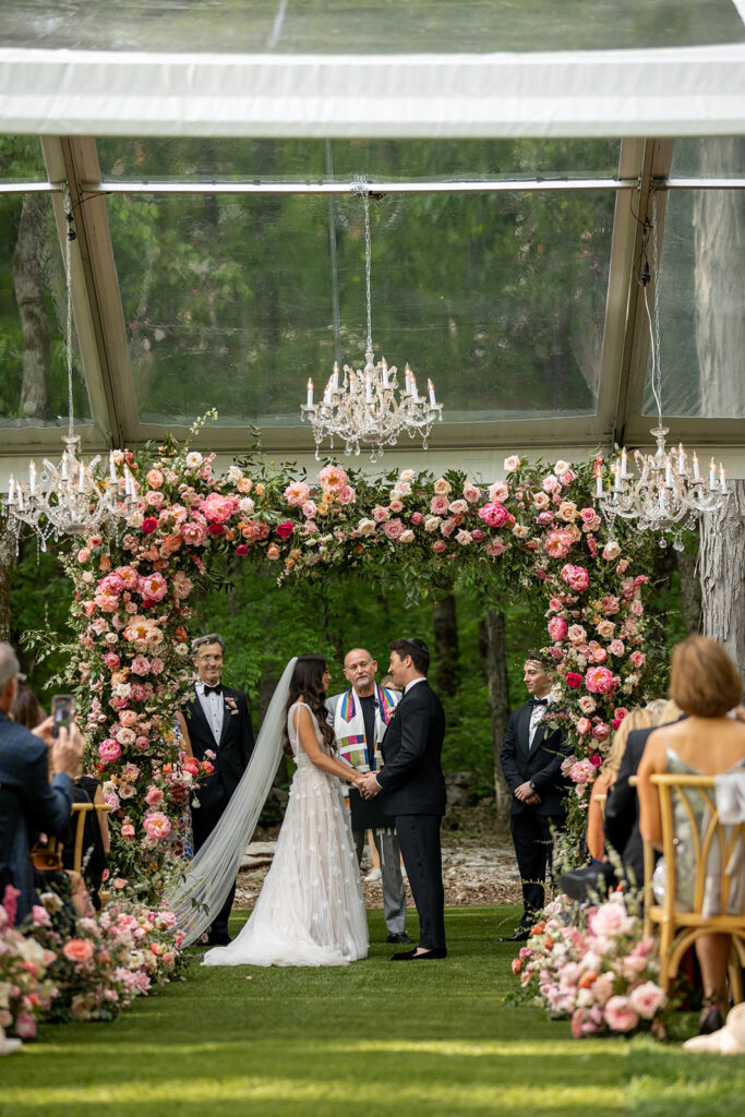 Spring wedding ceremony chuppah with lush pink peonies. Fun and vibrant floral design for spring wedding with roses, pink peonies, and natural greenery. Spring wedding in Tennessee countryside outside Nashville, TN. Design by Rosemary & Finch Floral Design in Nashville, TN.