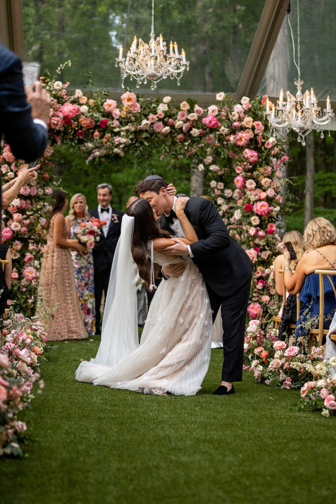 Spring wedding ceremony chuppah with lush pink peonies. Fun and vibrant floral design for spring wedding with roses, pink peonies, and natural greenery. Spring wedding in Tennessee countryside outside Nashville, TN. Design by Rosemary & Finch Floral Design in Nashville, TN.