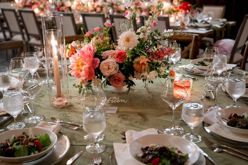 Low floral heavy centerpieces fill this spring wedding reception with fun floral colors. Pink florals at vibrant color to this spring wedding reception with pink peonies, roses, ranunculus, and pink tulips. Lush florals and pink candles decorate this epic pink head table. Destination wedding in Nashville countryside. Design by Rosemary & Finch Floral Design in Nashville, TN.