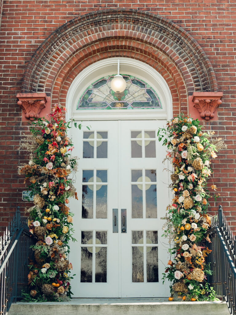 Church entrance floral installation for fall wedding in Franklin, TN. Broken arch florals for doors at church wedding ceremony. Fall wedding florals in dusty rose, caramel, honey, and copper. Floral photo moment for wedding ceremony exit. Destination wedding outside Nashville, TN. Design by Rosemary & Finch Floral Design in Nashville, TN. 