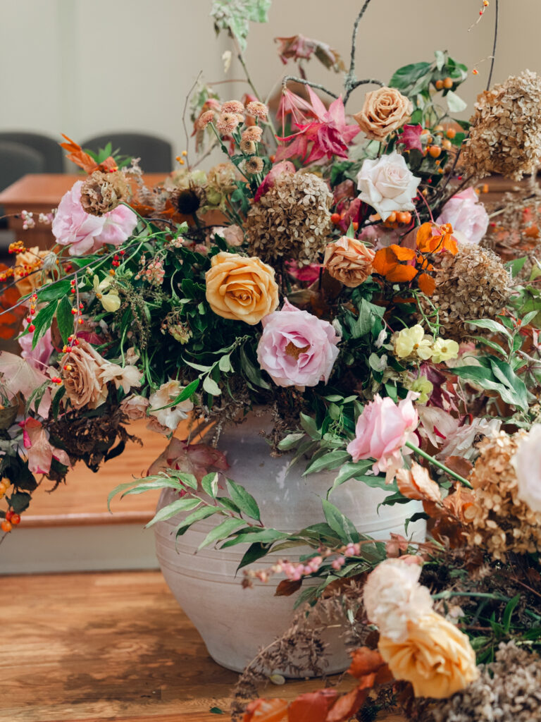 Large floral arrangements for ceremony backdrop. Staggered statement urn floral backdrop for fall wedding ceremony. Fall floral colors in dusty rose, copper, caramel, honey, and burgundy. Tasteful floral backdrop for church wedding ceremony with floral urns on either side. Destination wedding floral design for Nashville, TN. Design by Rosemary & Finch Floral Design in Nashville, TN. 