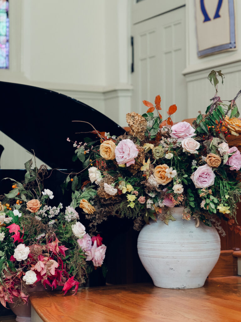 Large floral arrangements for ceremony backdrop. Staggered statement urn floral backdrop for fall wedding ceremony. Fall floral colors in dusty rose, copper, caramel, honey, and burgundy. Tasteful floral backdrop for church wedding ceremony with floral urns on either side. Destination wedding floral design for Nashville, TN. Design by Rosemary & Finch Floral Design in Nashville, TN. 