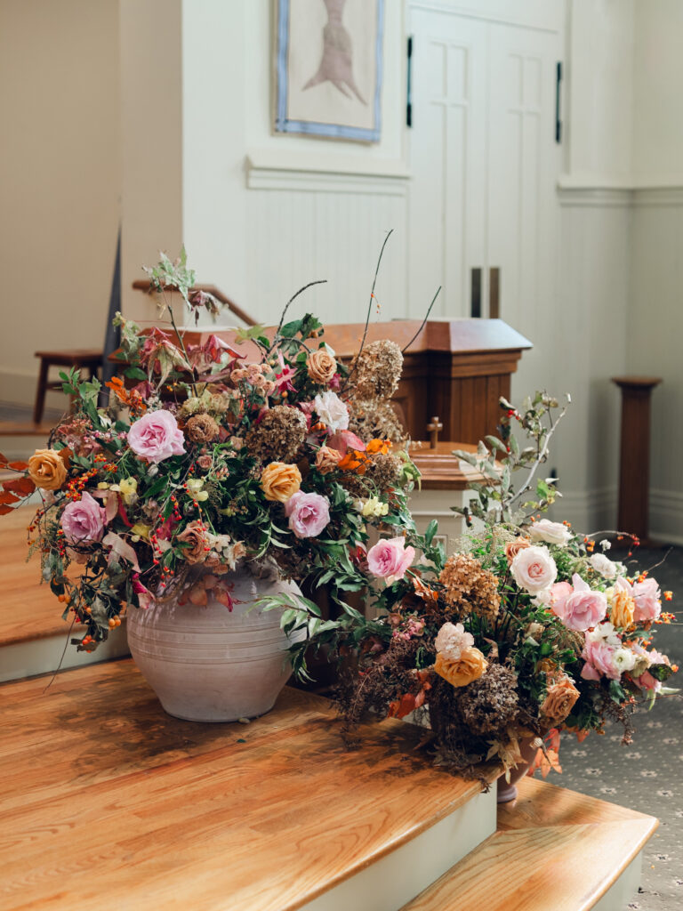 Large floral arrangements for ceremony backdrop. Staggered statement urn floral backdrop for fall wedding ceremony. Fall floral colors in dusty rose, copper, caramel, honey, and burgundy. Tasteful floral backdrop for church wedding ceremony with floral urns on either side. Destination wedding floral design for Nashville, TN. Design by Rosemary & Finch Floral Design in Nashville, TN. 