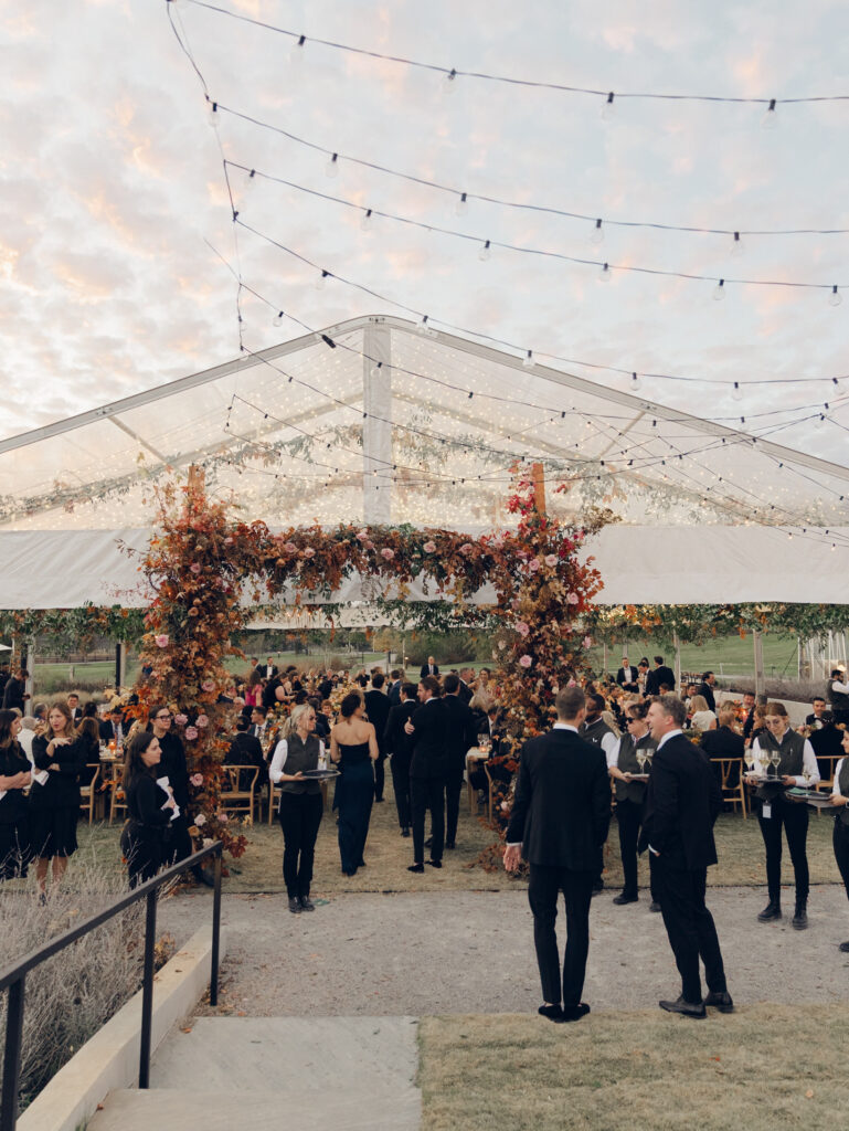 Tent entrance installation for fall wedding at Southall Farm & Inn. Lush floral install makes large impact in blush, tangerine, caramel, and mustard yellow flower colors. Large fall branches and roses make a statement for this wedding reception tent entrance. Destination floral design wedding outside Nashville, TN. Design by Rosemary & Finch Floral Design in Nashville, TN.