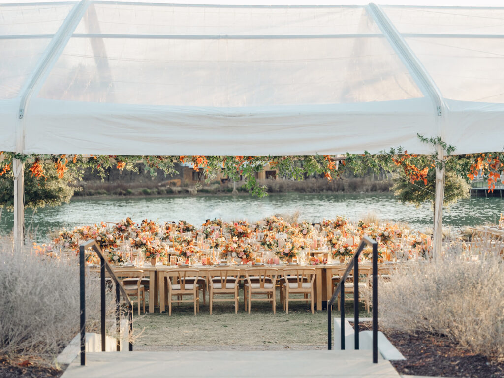 Full tablescapes of fall flowers create lush warm fall setting for wedding reception in Tennessee countryside. Wedding colors in blush, tangerine, mustard yellow, caramel, and honey. Wedding fall florals consisting of roses, clematis, ranunculus, brown tulips, and fall foliage. A collection of low centerpieces and accent arrangements create lush floral wedding reception tables with styled fruit place settings. Unique and colorful candles for reception tables in pink, orange, yellow, and gold. Destination floral design by Rosemary & Finch Floral Design in Nashville, TN.