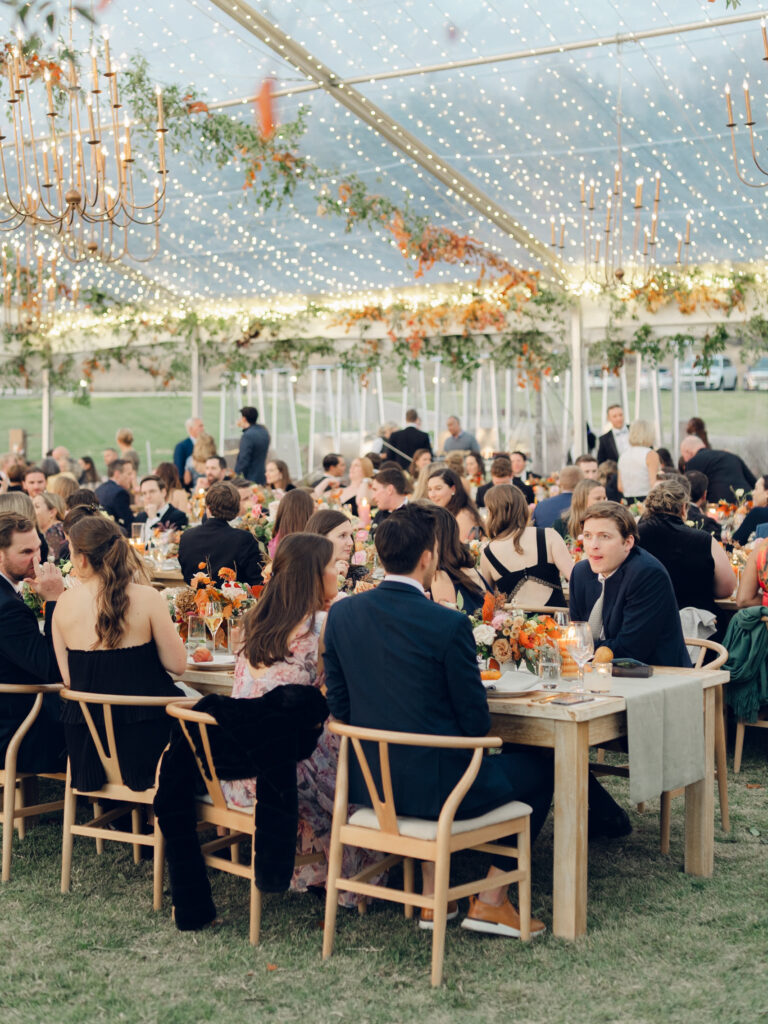 Full tablescapes of fall flowers create lush warm fall setting for wedding reception in Tennessee countryside. Wedding colors in blush, tangerine, mustard yellow, caramel, and honey. Wedding fall florals consisting of roses, clematis, ranunculus, brown tulips, and fall foliage. A collection of low centerpieces and accent arrangements create lush floral wedding reception tables with styled fruit place settings. Unique and colorful candles for reception tables in pink, orange, yellow, and gold. Destination floral design by Rosemary & Finch Floral Design in Nashville, TN.