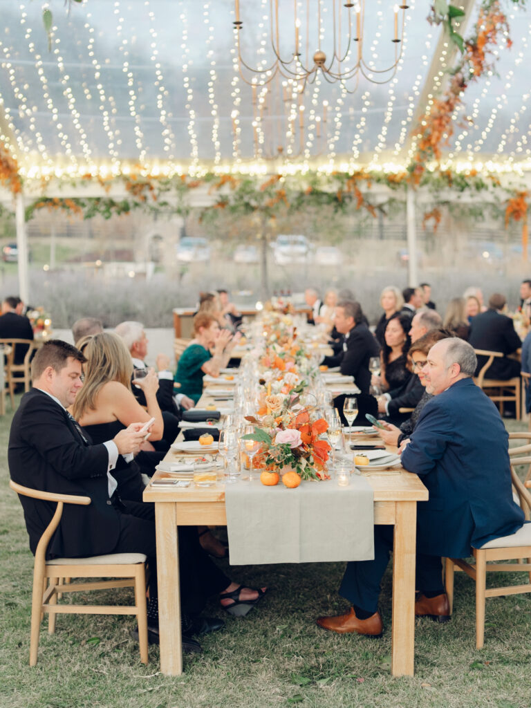 Full tablescapes of fall flowers create lush warm fall setting for wedding reception in Tennessee countryside. Wedding colors in blush, tangerine, mustard yellow, caramel, and honey. Wedding fall florals consisting of roses, clematis, ranunculus, brown tulips, and fall foliage. A collection of low centerpieces and accent arrangements create lush floral wedding reception tables with styled fruit place settings. Unique and colorful candles for reception tables in pink, orange, yellow, and gold. Destination floral design by Rosemary & Finch Floral Design in Nashville, TN.