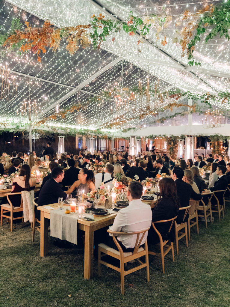 Full tablescapes of fall flowers create lush warm fall setting for wedding reception in Tennessee countryside. Wedding colors in blush, tangerine, mustard yellow, caramel, and honey. Wedding fall florals consisting of roses, clematis, ranunculus, brown tulips, and fall foliage. A collection of low centerpieces and accent arrangements create lush floral wedding reception tables with styled fruit place settings. Unique and colorful candles for reception tables in pink, orange, yellow, and gold. Destination floral design by Rosemary & Finch Floral Design in Nashville, TN.