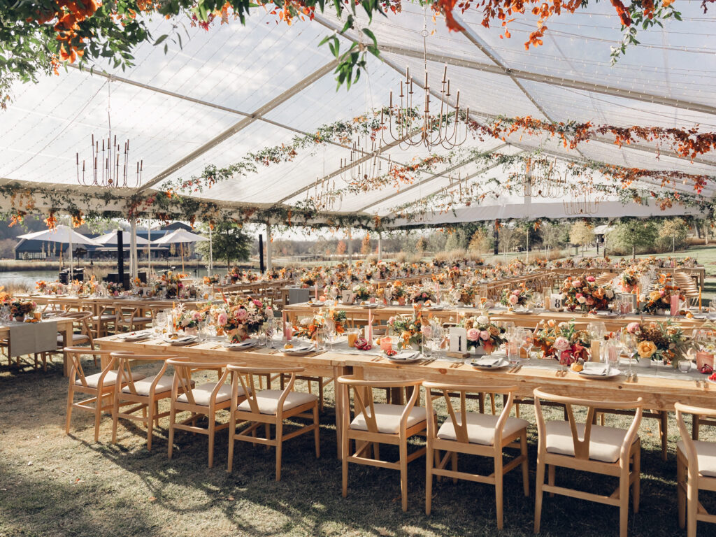 Full tablescapes of fall flowers create lush warm fall setting for wedding reception in Tennessee countryside. Wedding colors in blush, tangerine, mustard yellow, caramel, and honey. Wedding fall florals consisting of roses, clematis, ranunculus, brown tulips, and fall foliage. A collection of low centerpieces and accent arrangements create lush floral wedding reception tables with styled fruit place settings. Unique and colorful candles for reception tables in pink, orange, yellow, and gold. Destination floral design by Rosemary & Finch Floral Design in Nashville, TN.