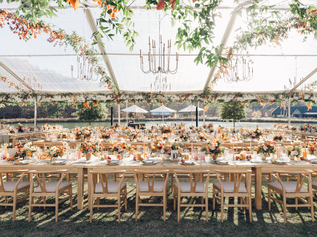 Full tablescapes of fall flowers create lush warm fall setting for wedding reception in Tennessee countryside. Wedding colors in blush, tangerine, mustard yellow, caramel, and honey. Wedding fall florals consisting of roses, clematis, ranunculus, brown tulips, and fall foliage. A collection of low centerpieces and accent arrangements create lush floral wedding reception tables with styled fruit place settings. Unique and colorful candles for reception tables in pink, orange, yellow, and gold. Destination floral design by Rosemary & Finch Floral Design in Nashville, TN.