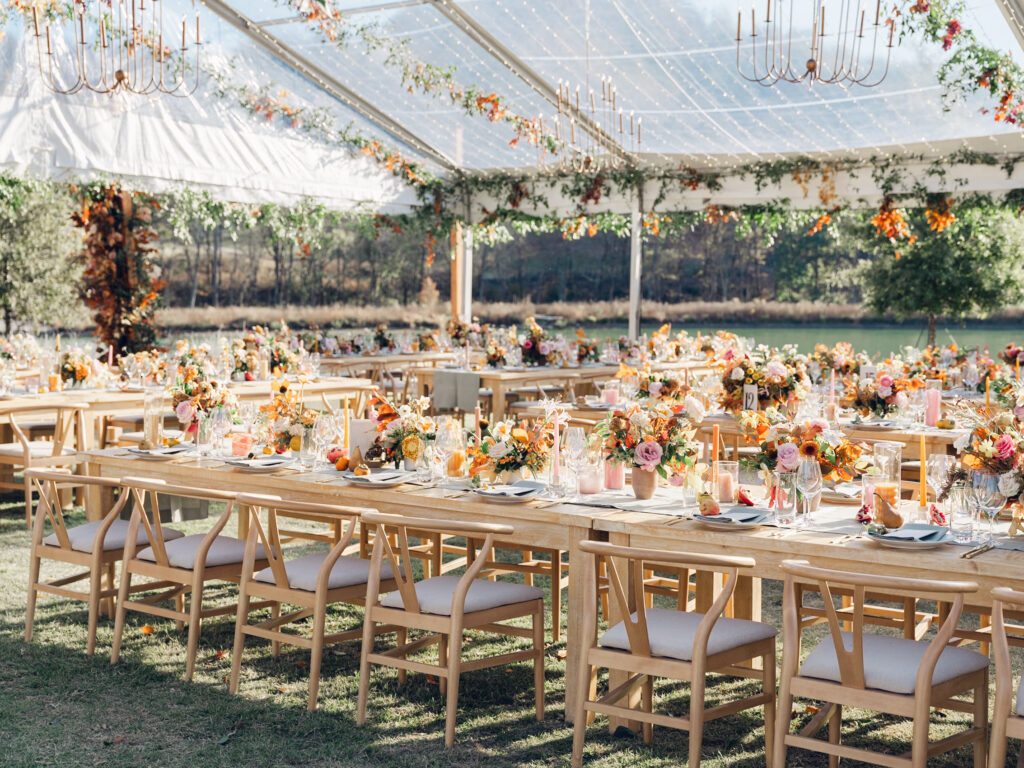 Full tablescapes of fall flowers create lush warm fall setting for wedding reception in Tennessee countryside. Wedding colors in blush, tangerine, mustard yellow, caramel, and honey. Wedding fall florals consisting of roses, clematis, ranunculus, brown tulips, and fall foliage. A collection of low centerpieces and accent arrangements create lush floral wedding reception tables with styled fruit place settings. Unique and colorful candles for reception tables in pink, orange, yellow, and gold. Destination floral design by Rosemary & Finch Floral Design in Nashville, TN.