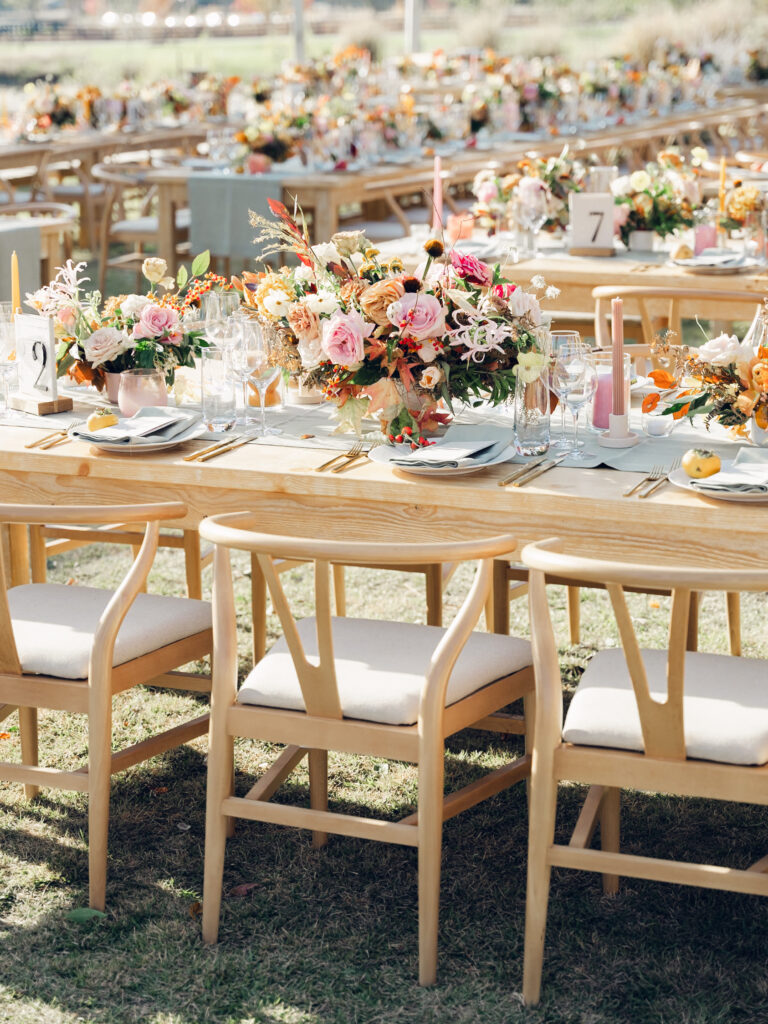 Full tablescapes of fall flowers create lush warm fall setting for wedding reception in Tennessee countryside. Wedding colors in blush, tangerine, mustard yellow, caramel, and honey. Wedding fall florals consisting of roses, clematis, ranunculus, brown tulips, and fall foliage. A collection of low centerpieces and accent arrangements create lush floral wedding reception tables with styled fruit place settings. Unique and colorful candles for reception tables in pink, orange, yellow, and gold. Destination floral design by Rosemary & Finch Floral Design in Nashville, TN.