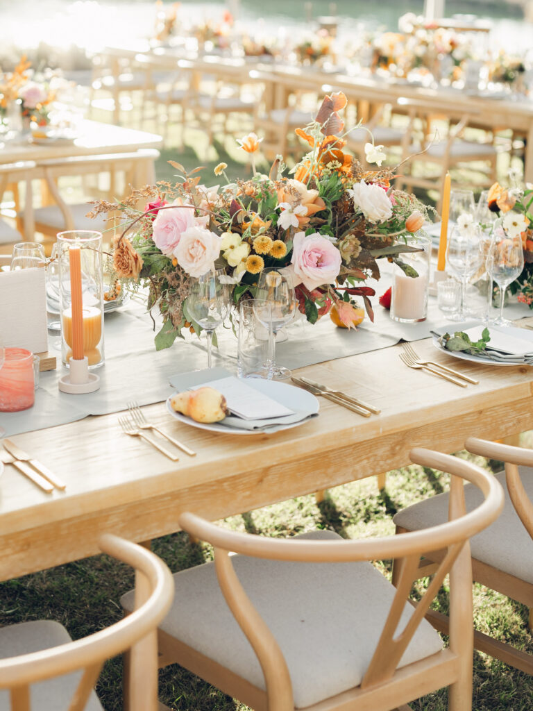 Full tablescapes of fall flowers create lush warm fall setting for wedding reception in Tennessee countryside. Wedding colors in blush, tangerine, mustard yellow, caramel, and honey. Wedding fall florals consisting of roses, clematis, ranunculus, brown tulips, and fall foliage. A collection of low centerpieces and accent arrangements create lush floral wedding reception tables with styled fruit place settings. Unique and colorful candles for reception tables in pink, orange, yellow, and gold. Destination floral design by Rosemary & Finch Floral Design in Nashville, TN.