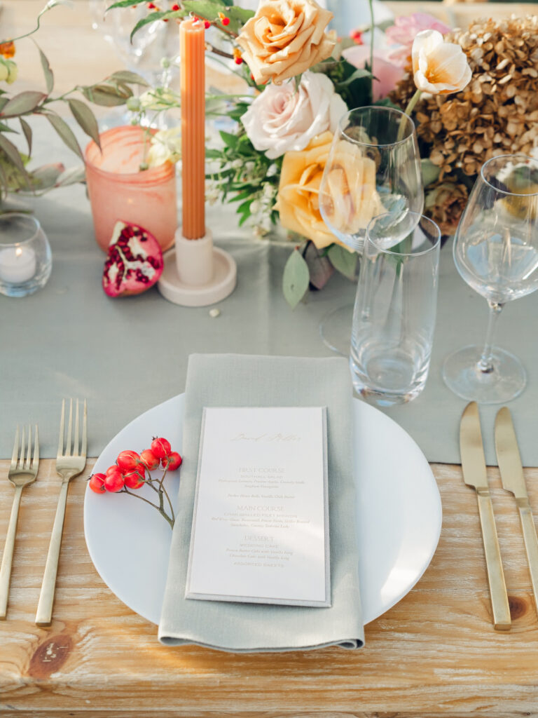 Full tablescapes of fall flowers create lush warm fall setting for wedding reception in Tennessee countryside. Wedding colors in blush, tangerine, mustard yellow, caramel, and honey. Wedding fall florals consisting of roses, clematis, ranunculus, brown tulips, and fall foliage. A collection of low centerpieces and accent arrangements create lush floral wedding reception tables with styled fruit place settings. Unique and colorful candles for reception tables in pink, orange, yellow, and gold. Destination floral design by Rosemary & Finch Floral Design in Nashville, TN.