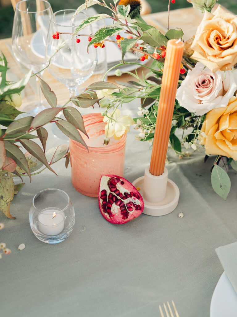 Full tablescapes of fall flowers create lush warm fall setting for wedding reception in Tennessee countryside. Wedding colors in blush, tangerine, mustard yellow, caramel, and honey. Wedding fall florals consisting of roses, clematis, ranunculus, brown tulips, and fall foliage. A collection of low centerpieces and accent arrangements create lush floral wedding reception tables with styled fruit place settings. Unique and colorful candles for reception tables in pink, orange, yellow, and gold. Destination floral design by Rosemary & Finch Floral Design in Nashville, TN.