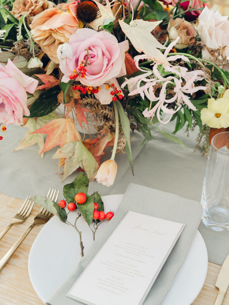 Full tablescapes of fall flowers create lush warm fall setting for wedding reception in Tennessee countryside. Wedding colors in blush, tangerine, mustard yellow, caramel, and honey. Wedding fall florals consisting of roses, clematis, ranunculus, brown tulips, and fall foliage. A collection of low centerpieces and accent arrangements create lush floral wedding reception tables with styled fruit place settings. Unique and colorful candles for reception tables in pink, orange, yellow, and gold. Destination floral design by Rosemary & Finch Floral Design in Nashville, TN.