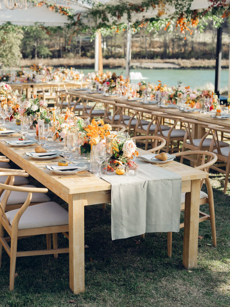 Full tablescapes of fall flowers create lush warm fall setting for wedding reception in Tennessee countryside. Wedding colors in blush, tangerine, mustard yellow, caramel, and honey. Wedding fall florals consisting of roses, clematis, ranunculus, brown tulips, and fall foliage. A collection of low centerpieces and accent arrangements create lush floral wedding reception tables with styled fruit place settings. Unique and colorful candles for reception tables in pink, orange, yellow, and gold. Destination floral design by Rosemary & Finch Floral Design in Nashville, TN.