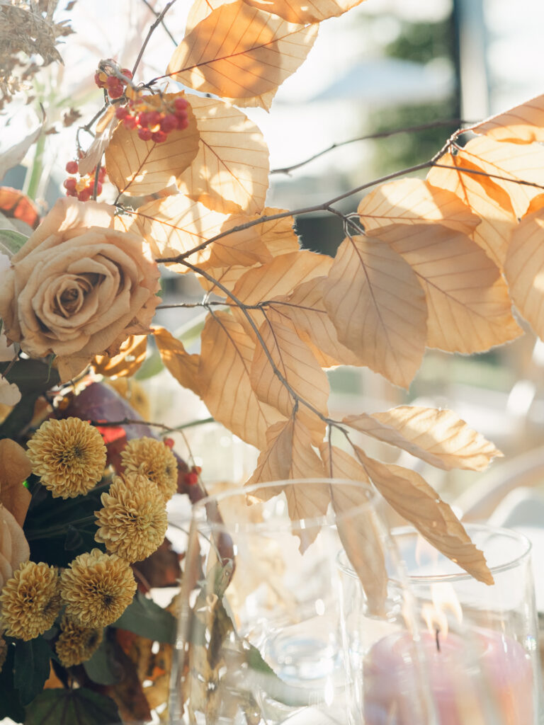 Full tablescapes of fall flowers create lush warm fall setting for wedding reception in Tennessee countryside. Wedding colors in blush, tangerine, mustard yellow, caramel, and honey. Wedding fall florals consisting of roses, clematis, ranunculus, brown tulips, and fall foliage. A collection of low centerpieces and accent arrangements create lush floral wedding reception tables with styled fruit place settings. Unique and colorful candles for reception tables in pink, orange, yellow, and gold. Destination floral design by Rosemary & Finch Floral Design in Nashville, TN.