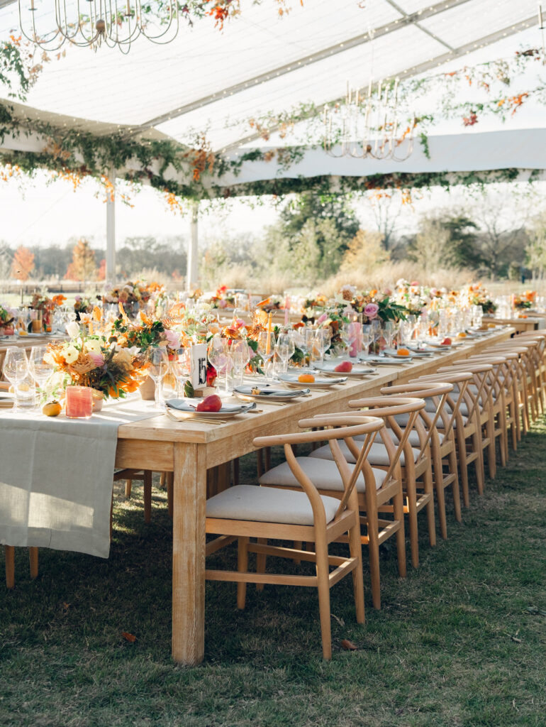 Full tablescapes of fall flowers create lush warm fall setting for wedding reception in Tennessee countryside. Wedding colors in blush, tangerine, mustard yellow, caramel, and honey. Wedding fall florals consisting of roses, clematis, ranunculus, brown tulips, and fall foliage. A collection of low centerpieces and accent arrangements create lush floral wedding reception tables with styled fruit place settings. Unique and colorful candles for reception tables in pink, orange, yellow, and gold. Destination floral design by Rosemary & Finch Floral Design in Nashville, TN.