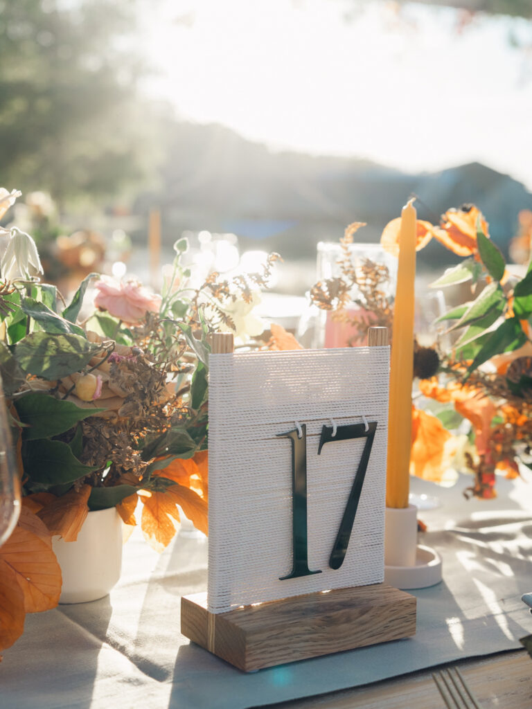 Full tablescapes of fall flowers create lush warm fall setting for wedding reception in Tennessee countryside. Wedding colors in blush, tangerine, mustard yellow, caramel, and honey. Wedding fall florals consisting of roses, clematis, ranunculus, brown tulips, and fall foliage. A collection of low centerpieces and accent arrangements create lush floral wedding reception tables with styled fruit place settings. Unique and colorful candles for reception tables in pink, orange, yellow, and gold. Destination floral design by Rosemary & Finch Floral Design in Nashville, TN.