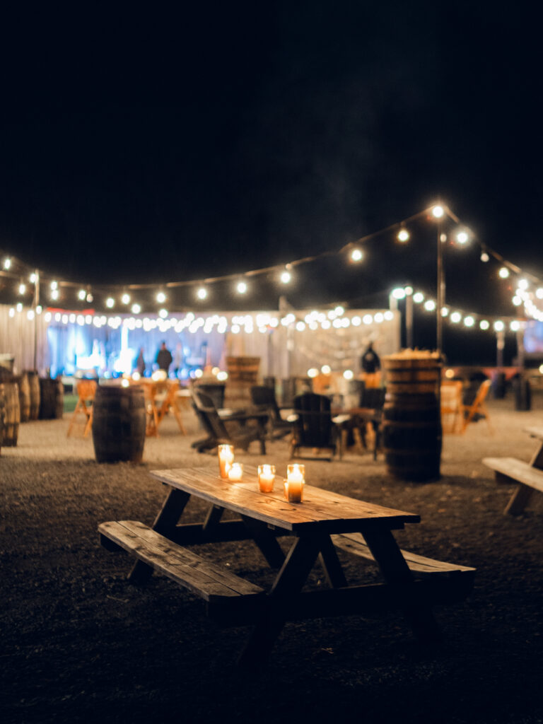 Fall wedding welcome party illuminated by amber glass pillar candles for rustic vibes in Tennessee countryside destination wedding. Warm romantic lighting for wedding weekend welcome party at whiskey distillery. Design by Rosemary & Finch Floral Design in Nashville, TN. 