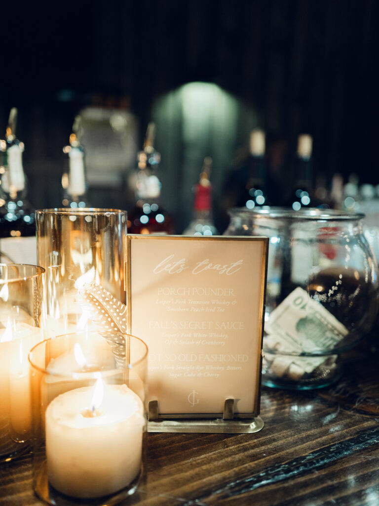 Fall wedding welcome party illuminated by amber glass pillar candles for rustic vibes in Tennessee countryside destination wedding. Warm romantic lighting for wedding weekend welcome party at whiskey distillery. Design by Rosemary & Finch Floral Design in Nashville, TN. 