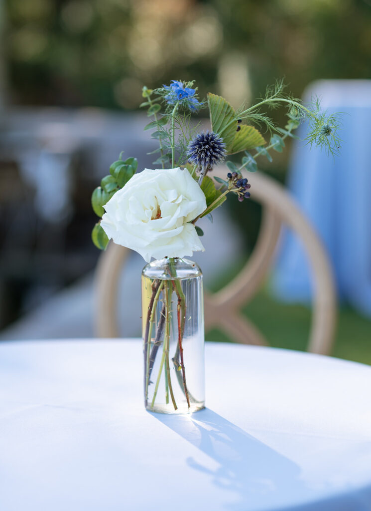 Outdoor wedding reception florals for cocktail hour. Bud vases for cocktail hour with summer wildflowers. Blue and white wedding florals for summer wedding decorate the cocktail hour bar for outdoor wedding reception. Elevated floral arrangements for outdoor lounge area. Design by Rosemary & Finch in Nashville, TN.