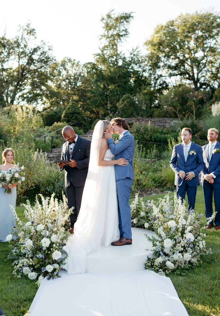 Floral ground meadow for summer wedding ceremony. Blue and white wedding ceremony florals consisting of roses, delphinium, thistle, spirea, and natural greenery. Tall ground floral arch surrounding bride and groom in outdoor garden-inspired wedding. Design by Rosemary & Finch Floral Design in Nashville, TN. 