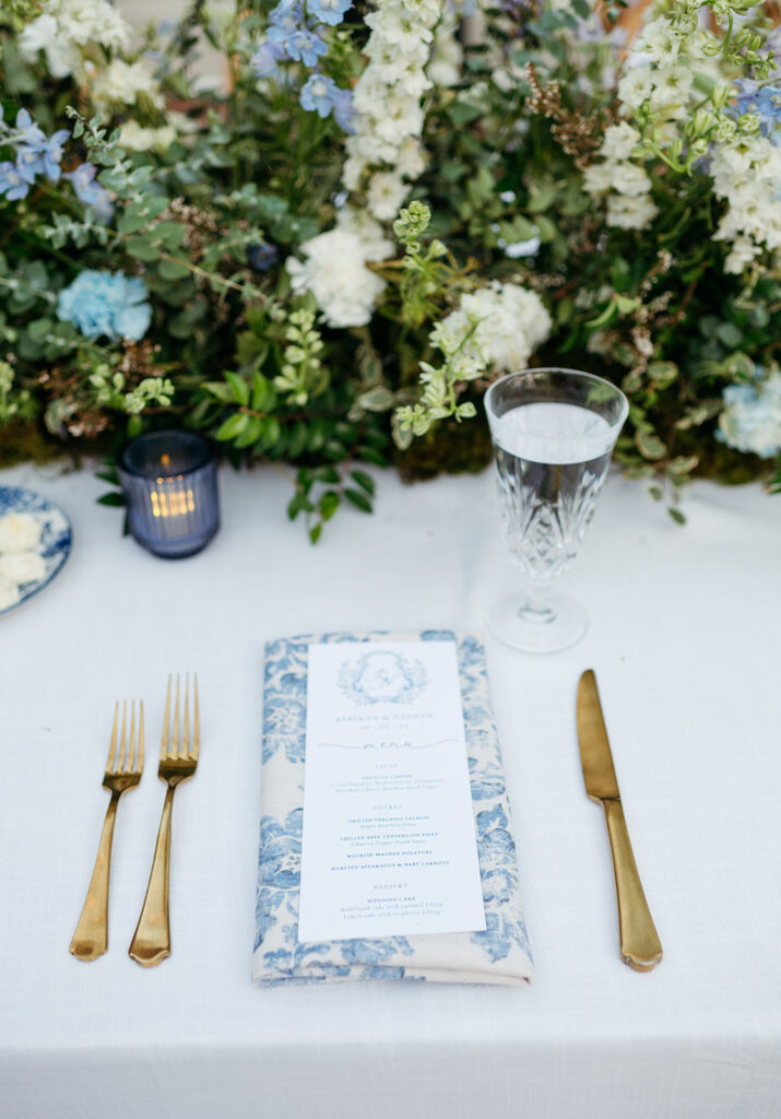 Long floral meadows line the head tables of this garden-inspired wedding at Cheekwood. Lush floral centerpieces in blue and white for summer wedding reception. White wedding florals with hint of blue consisting of white and blue delphinium. Clear and dusty blue candles add warm lighting for outdoor wedding reception. Floral table runner for wedding reception head tables. Design by Rosemary & Finch Floral Design in Nashville, TN.