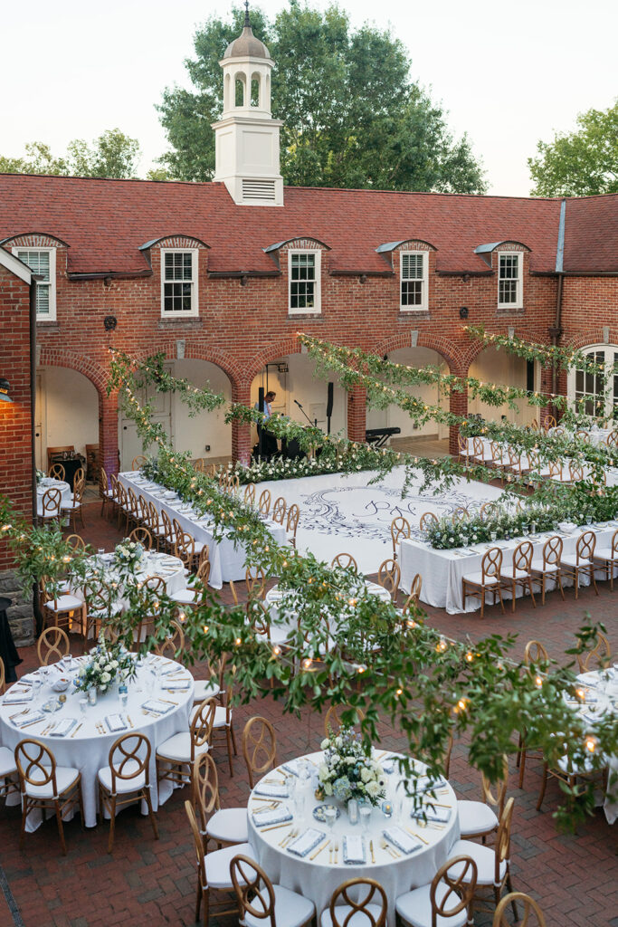 Garden-inspired summer wedding reception at Cheekwood. Summer wedding florals in blue and white consisting of roses, blue tulips, delphinium, carnations, and natural greenery. String lights with greenery over courtyard wedding reception. Italian inspired courtyard wedding for outdoor summer reception. Design by Rosemary & Finch Floral Design in Nashville, TN.   