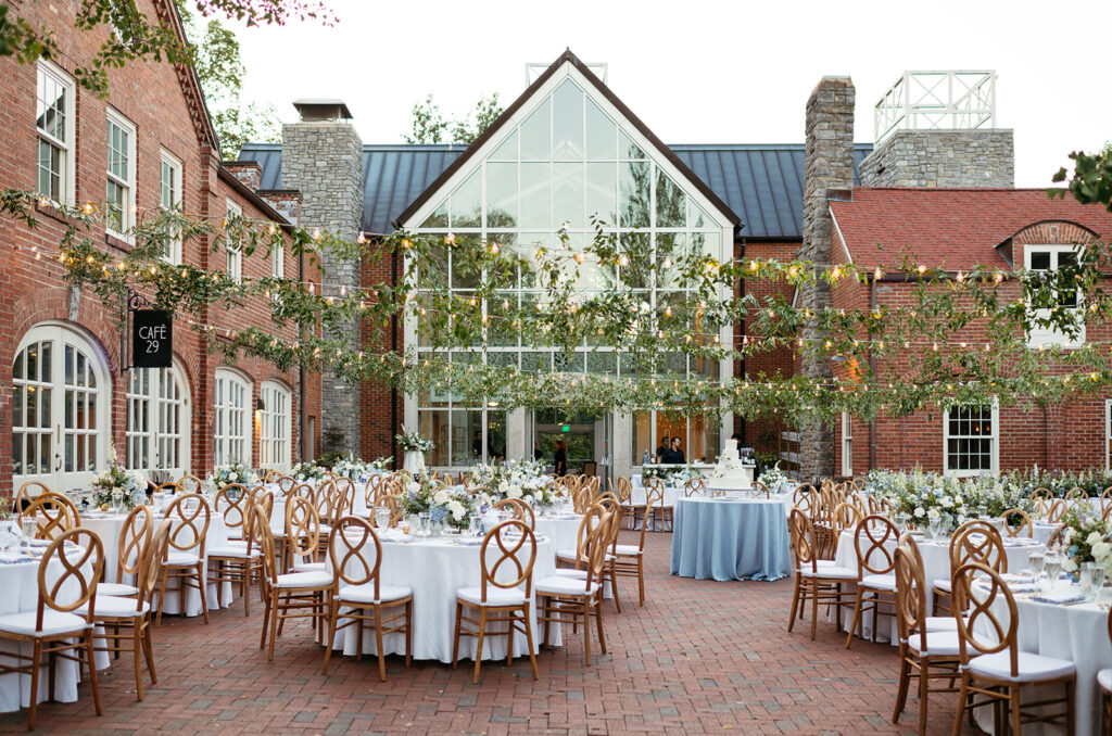 Garden-inspired summer wedding reception at Cheekwood. Summer wedding florals in blue and white consisting of roses, blue tulips, delphinium, carnations, and natural greenery. String lights with greenery over courtyard wedding reception. Italian inspired courtyard wedding for outdoor summer reception. Design by Rosemary & Finch Floral Design in Nashville, TN.   