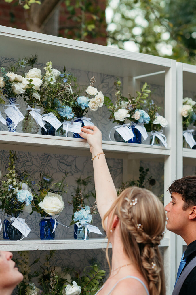 Bud Vase escort display in colors blue and white for summer wedding reception. Antique blue and white vases decorate summer wedding escort display with roses, ranunculus, carnations, and greenery. Escort display with floral party favors for guests. Italian inspired wedding reception with vintage blue and white floral vases. Design by Rosemary & Finch in Nashville, TN. 