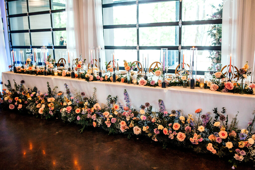 Lush floral head table for wedding reception in Nashville, TN. Colorful and fun wedding flowers for summer wedding reception. Florals running along the base of the head table for wedding reception with table floral garland. Fun colorful wedding candles. Design by Rosemary & Finch in Nashville, TN.