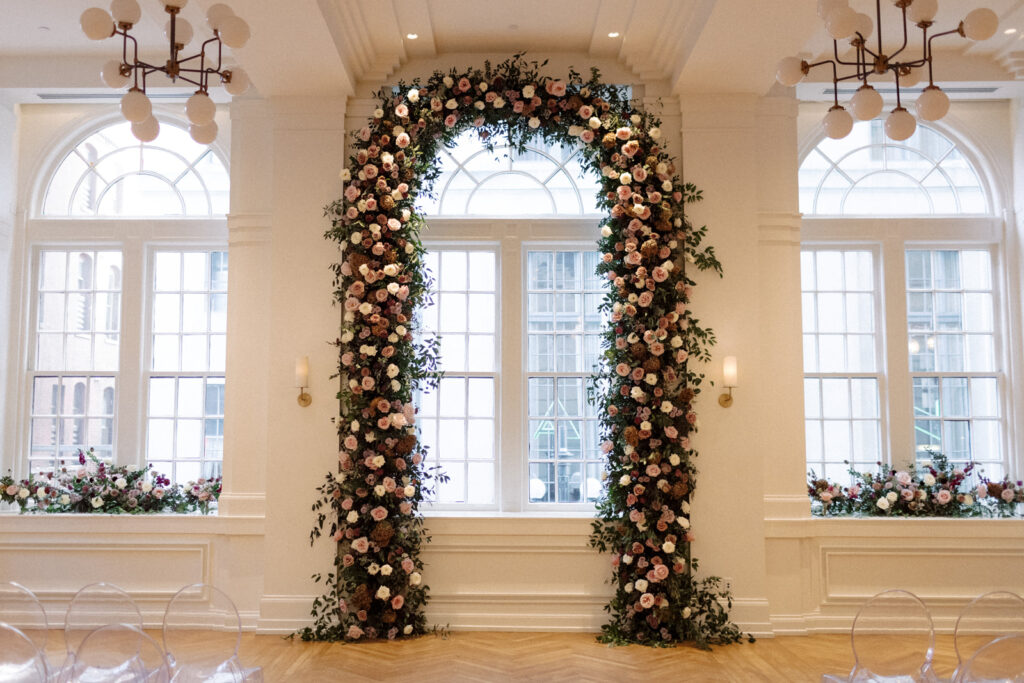 Large window floral arch for wedding ceremony and reception. Fall wedding in downtown Nashville with purple wedding colors. Flowers in mauve, eggplant, plum, and cream. Roses, scabiosa, berries, and branches. Floral textures for fall wedding. Design by Rosemary & Finch Floral Design in Nashville, TN. 