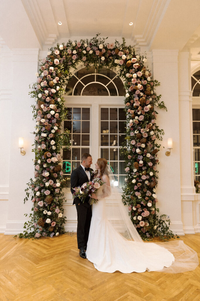 Large window floral arch for wedding ceremony and reception. Fall wedding in downtown Nashville with purple wedding colors. Flowers in mauve, eggplant, plum, and cream. Roses, scabiosa, berries, and branches. Floral textures for fall wedding. Design by Rosemary & Finch Floral Design in Nashville, TN. 