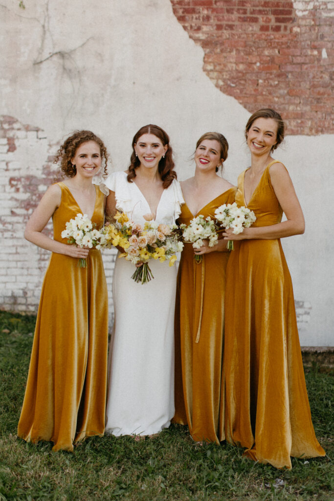 Artful bridal bouquet in yellow tones with cream accents brings unique floral design to fall wedding. Dainty blooms of tulips, spray roses, butterfly ranunculus create colorful fall floral design. Wedding party florals for fall wedding in unique yellow, cream, and toffee colors. Urban fall wedding with modern romantic details. Destination wedding floral designer. Design by Rosemary & Finch Floral Design in Nashville, TN. 