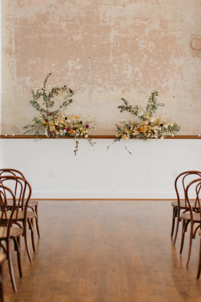 Whimsical and unique florals for urban wedding ceremony. Growing floral meadows for fall wedding ceremony backdrop. Natural growing greenery and florals create artful backdrop for indoor wedding ceremony. Fall wedding floral design in tones of yellow, cream, and toffee. Urban fall wedding with modern romantic details. Design by Rosemary & Finch Floral Design in Nashville, TN.