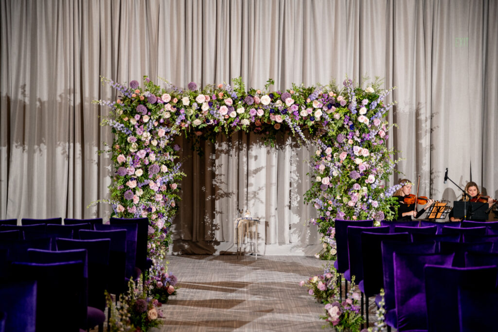 Lush floral chuppah in hues of lavender, plush, plum, and cream for fall wedding ceremony. Aisle adorned with floral ground meadows at the base of each chair. Wildflowers, roses, and growing greenery for fall wedding florals. Unique purple wedding colors for fall wedding ceremony. Design by Rosemary & Finch Floral Design in Nashville, TN. 
