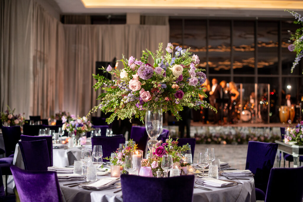 Lush florals for elevated centerpieces for fall wedding reception tables. Lavender and purple color scheme for fall wedding at the Four Seasons Hotel. Floral colors in lavender, blush, mauve, and rose. Unique and fun candles in purple tones decorate dinner tables. Design by Rosemary & Finch Floral Design in Nashville, TN. 