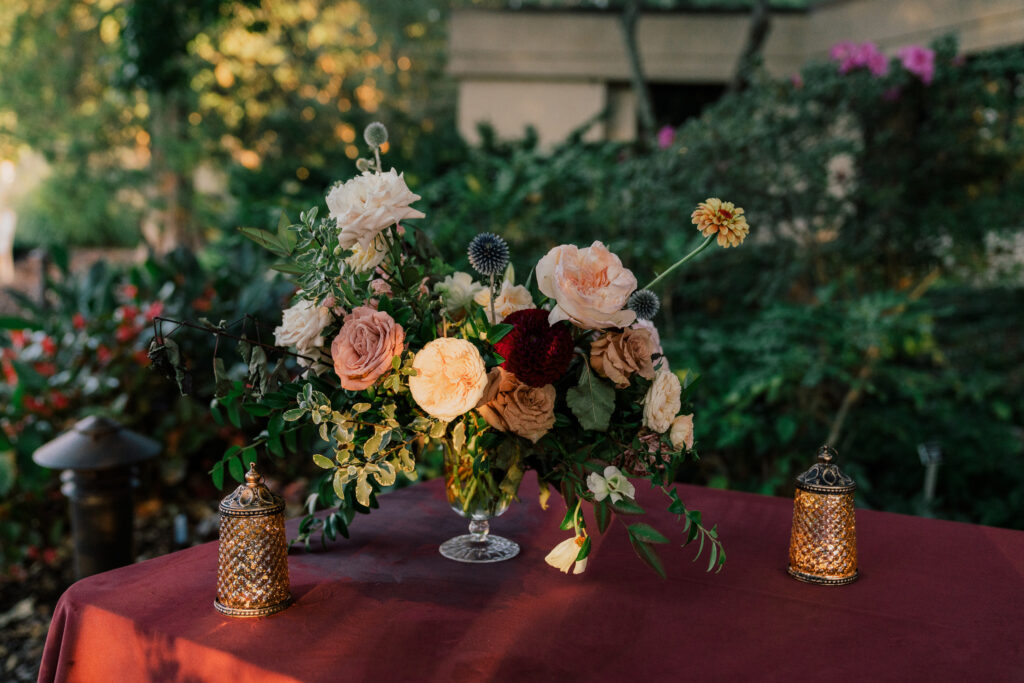 Fall wedding florals for cocktail hour. Bud vases and bar florals decorate this outdoor cocktail hour in fall colors. Fall floral colors with touches of pink, golden yellow, blue, and burgundy. Local fall flowers of zinnias, dahlias, and roses for fall wedding. Destination floral designer for travel weddings. Design by Rosemary & Finch Floral Design in Nashville, TN.