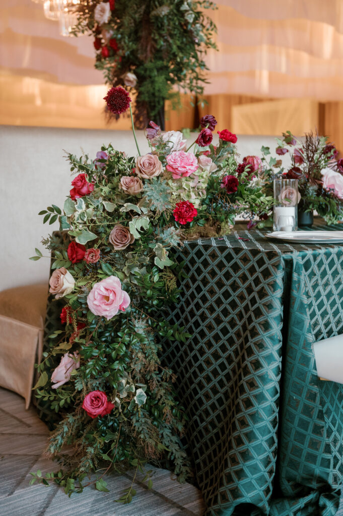 Standing chandeliers covered in lush florals for winter wedding at the Four Seasons. Jewel tone wedding reception florals with reception table floral cascades and table meadows. Winter floral colors in ruby, blush, plum, and magenta. Accent arrangement runners for wedding reception tablescapes. Design by Rosemary & Finch Floral Design.