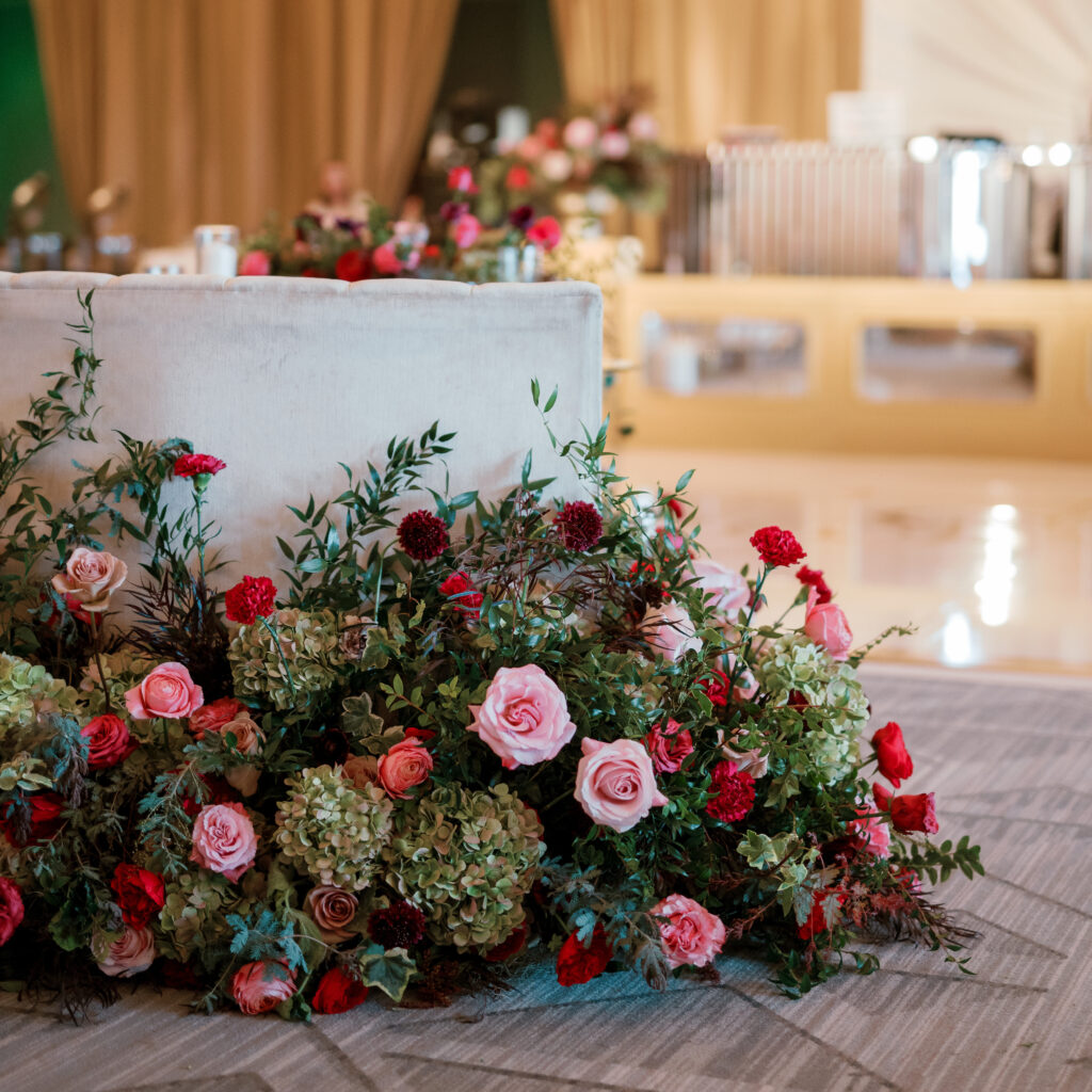 Sweetheart table surrounded by floral meadows in wedding reception. Moody jewel tone wedding reception florals in ruby, blush, plum, and magenta. Winter wedding reception at the Four Seasons. Lush floral moment for wedding sweetheart table. Design by Rosemary & Finch Floral Design. 