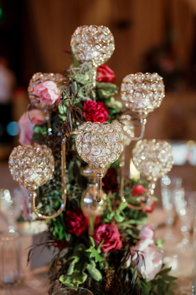 Candelabra with florals surrounding base on wedding tables. Lush florals on crystal candles in for winter wedding reception. Moody jewel tone wedding reception florals in ruby, blush, plum, and magenta. Unique wedding reception centerpieces. Wedding reception in Downtown Nashville at the Four Seasons. Design by Rosemary & Finch Floral Design.