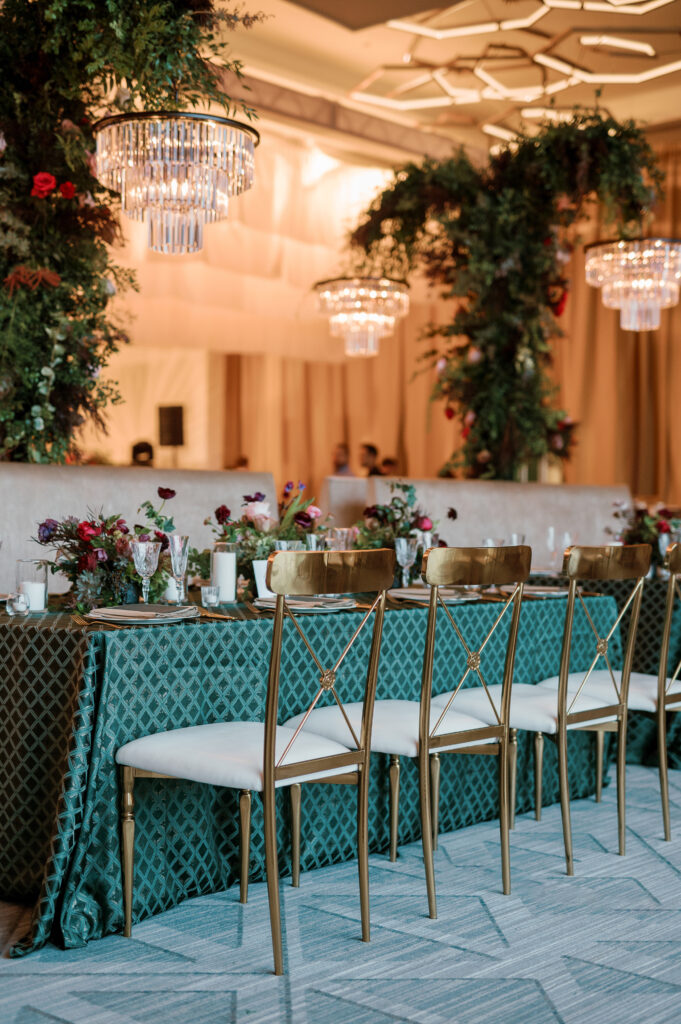 Standing chandeliers covered in lush florals for winter wedding at the Four Seasons. Jewel tone wedding reception florals with reception table floral cascades and table meadows. Winter floral colors in ruby, blush, plum, and magenta. Accent arrangement runners for wedding reception tablescapes. Design by Rosemary & Finch Floral Design.