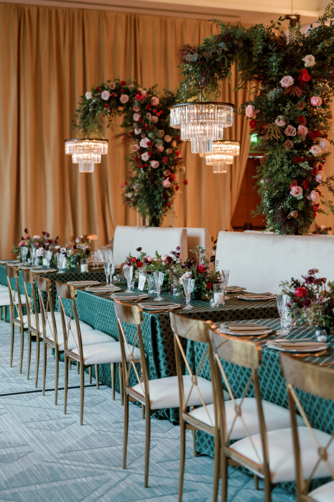 Standing chandeliers covered in lush florals for winter wedding at the Four Seasons. Jewel tone wedding reception florals with reception table floral cascades and table meadows. Winter floral colors in ruby, blush, plum, and magenta. Accent arrangement runners for wedding reception tablescapes. Design by Rosemary & Finch Floral Design.