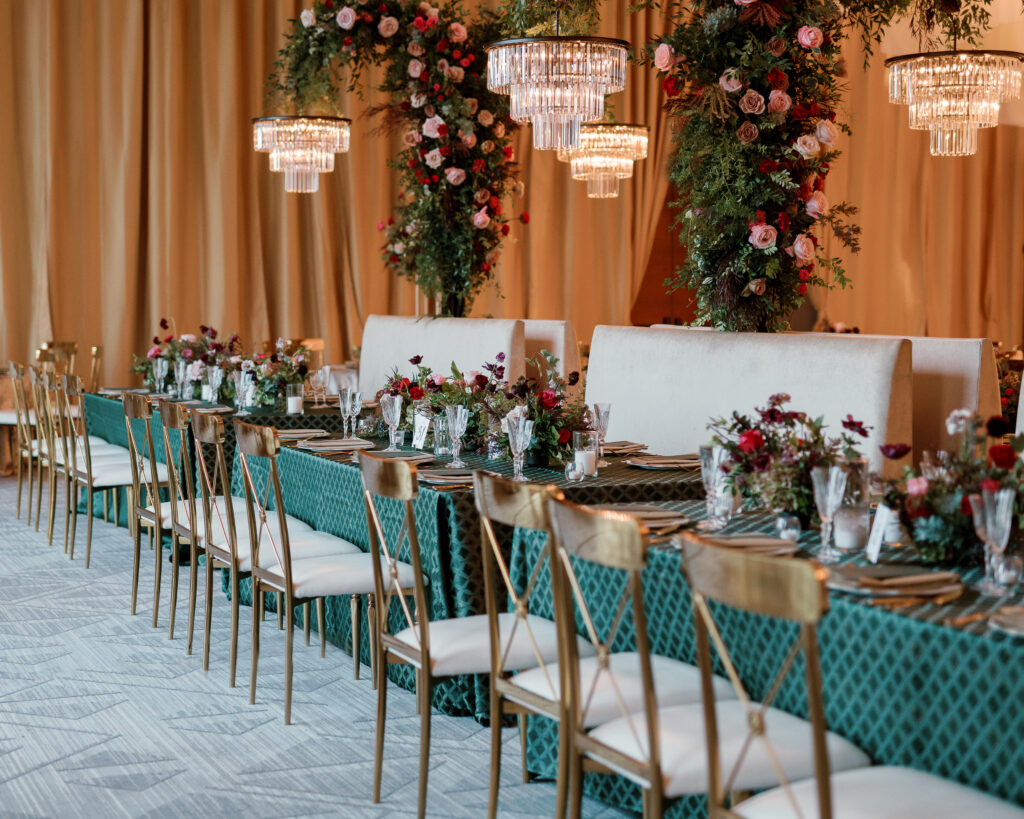 Standing chandeliers covered in lush florals for winter wedding at the Four Seasons. Jewel tone wedding reception florals with reception table floral cascades and table meadows. Winter floral colors in ruby, blush, plum, and magenta. Accent arrangement runners for wedding reception tablescapes. Design by Rosemary & Finch Floral Design.